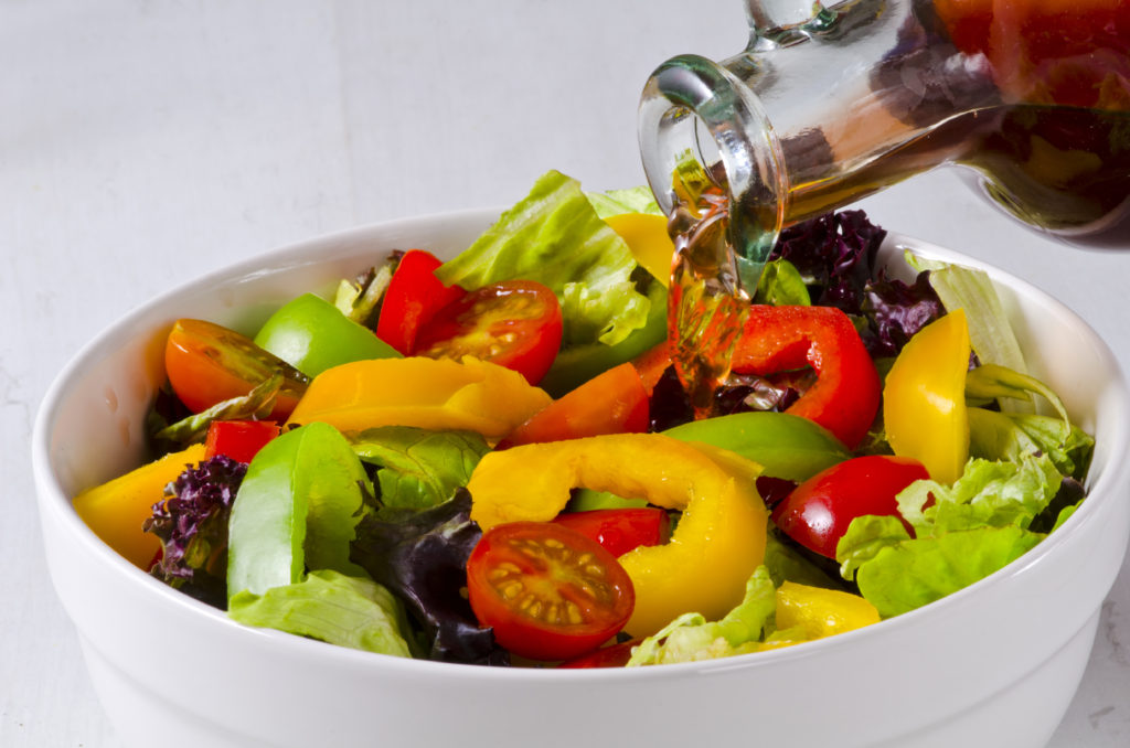 Vinegar pouring into fresh salad bowl. White background.